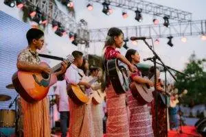 Youth band with guitars performing live on stage during an outdoor cultural event at sunset.