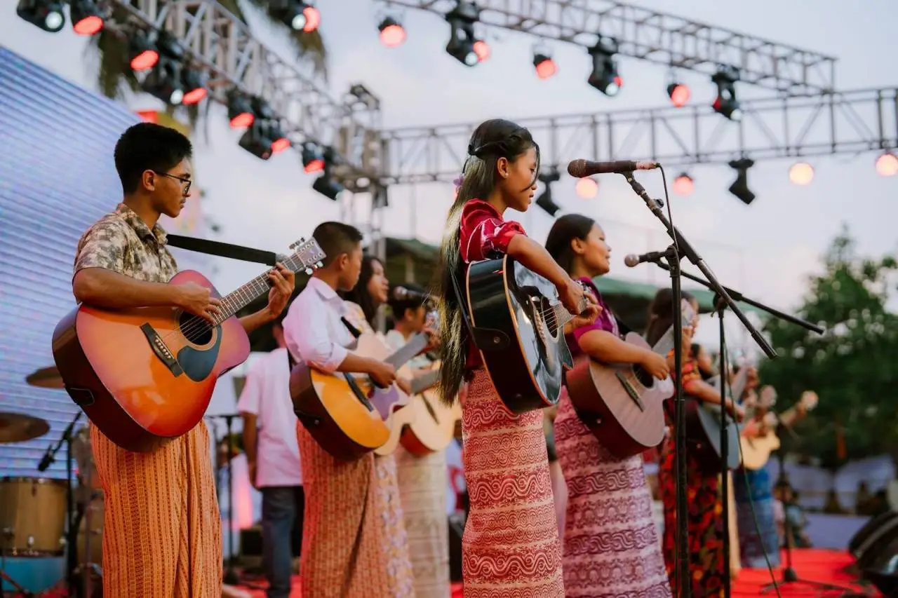 Youth band with guitars performing live on stage during an outdoor cultural event at sunset.