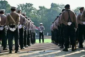 A group of police officers stands in formation outdoors, observed from behind, during a formal event.