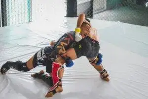 Two athletes engage in a dynamic mixed martial arts sparring match in an indoor training cage.