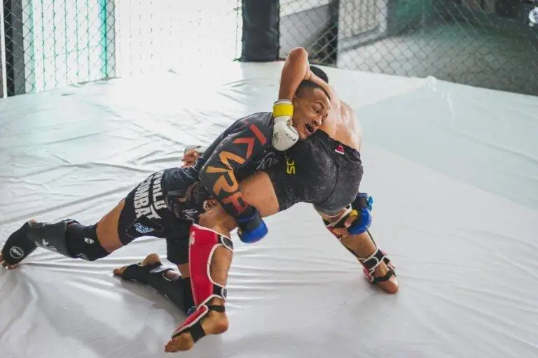 Two athletes engage in a dynamic mixed martial arts sparring match in an indoor training cage.